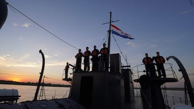 Seis personas uniformadas y con chalecos salvavidas en el barco, con la bandera de Paraguay ondeando al fondo.