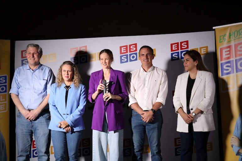 Soledad Núñez en el centro, con micrófono, rodeada de cuatro personas sonriendo en evento interior con logo 'ES SOL'.