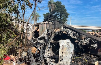 Vehículo dañado tras accidente, rodeado de árboles y vegetación, con resto metálico expuesto y signos de incendio.
