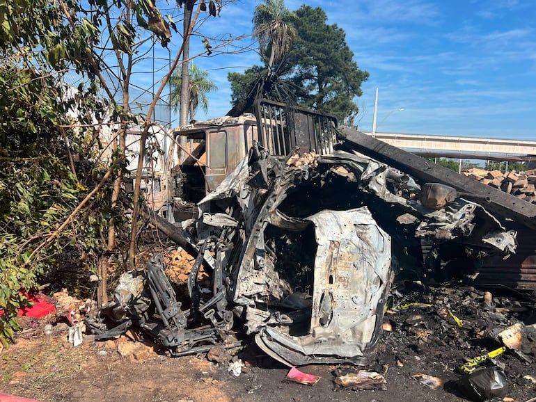 Vehículo dañado tras accidente, rodeado de árboles y vegetación, con resto metálico expuesto y signos de incendio.