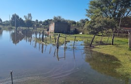 Paisaje rural inundado, con una construcción de ladrillo y cercas de madera parcialmente sumergidas.