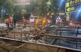 Trabajador con casco amarillo y chaleco naranja manipula estructura metálica con varios colegas en una obra pública.