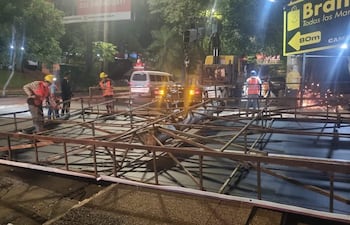 Trabajador con casco amarillo y chaleco naranja manipula estructura metálica con varios colegas en una obra pública.
