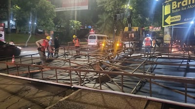 Trabajador con casco amarillo y chaleco naranja manipula estructura metálica con varios colegas en una obra pública.