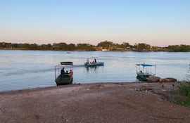 Barco de carga verde atracado, con una persona de pie en la cubierta y objetos visibles en un entorno natural.