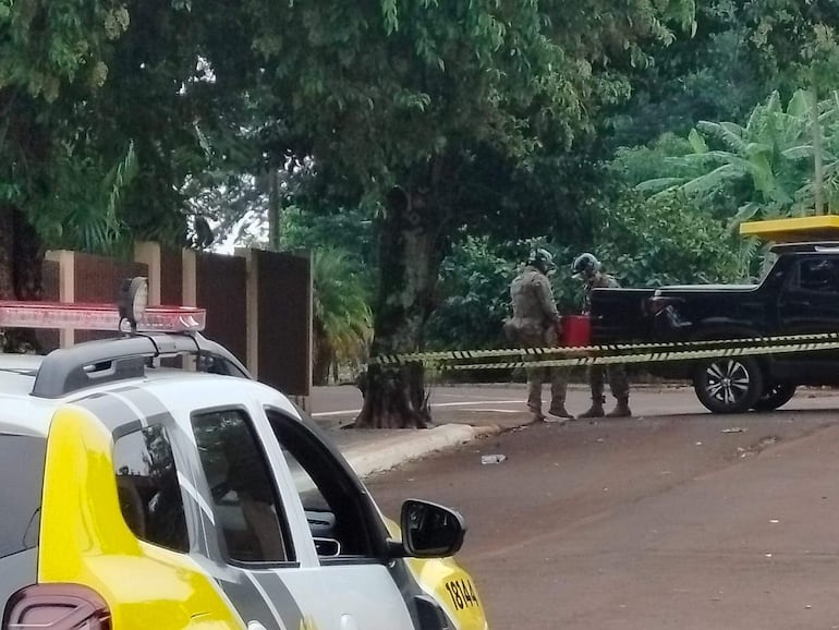 Dos miembros de seguridad con uniformes camuflados junto a camioneta negra, sosteniendo un recipiente rojo en un área boscosa.