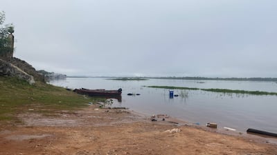 Bote de madera sobre la orilla del río Paraguay, rodeado de vegetación y un paisaje acuático nublado.