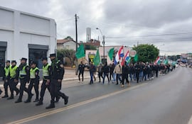 Grupo de campesinos marchan con banderas en una calle, bajo un clima fresco, con la presencia de policías que acompañan la manifestación.