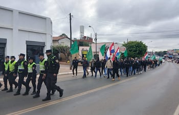 Grupo de campesinos marchan con banderas en una calle, bajo un clima fresco, con la presencia de policías que acompañan la manifestación.
