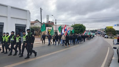 Grupo de campesinos marchan con banderas en una calle, bajo un clima fresco, con la presencia de policías que acompañan la manifestación.