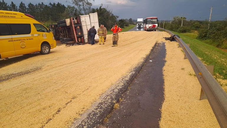 Cuatro trabajadores en la escena del accidente, con uniformes, ayudando tras el vuelco de un camión cargado de soja en la carretera.