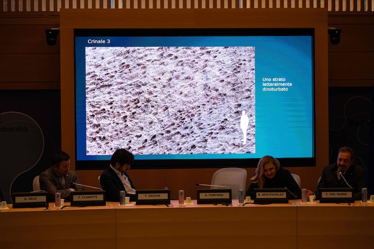 El paleontólogo del Museo de Historia Natural de Milán, Cristiano Dal Sasso (der.), comenta fotografías proyectadas en una pantalla durante una conferencia de prensa para presentar el descubrimiento de miles de huellas de dinosaurios halladas en el Parque Nacional del Stelvio, en Italia, cerca de las zonas que albergarán los Juegos Olímpicos de Milán-Cortina 2026, en Milán, el 16 de diciembre de 2025.