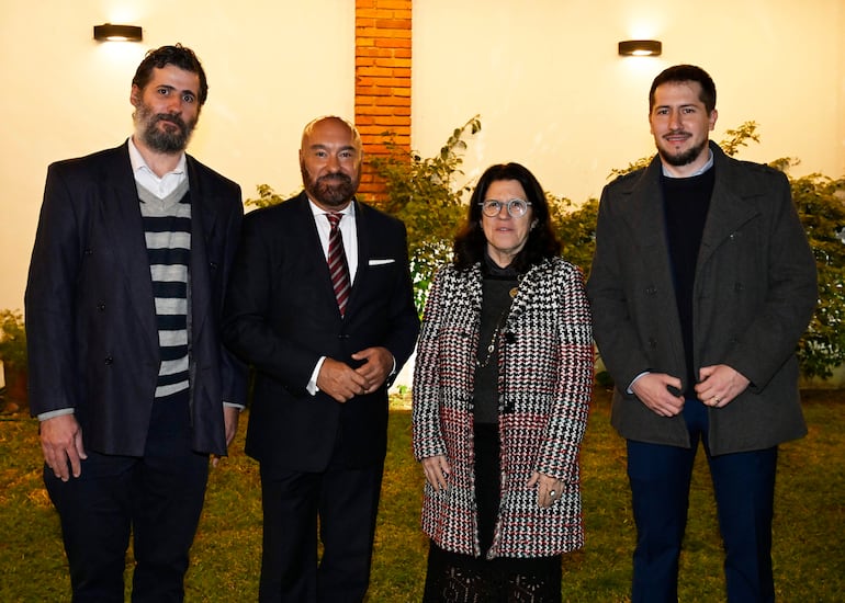 Pierre-Christian Soccoja y tres adultos posan, luciendo abrigos y chaquetas, en un ambiente exterior iluminado con luz suave.