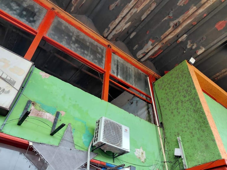 Edificio deteriorado con ventanas de marcos rojos y paredes verdes desgastadas, reflejando abandono en la terminal.