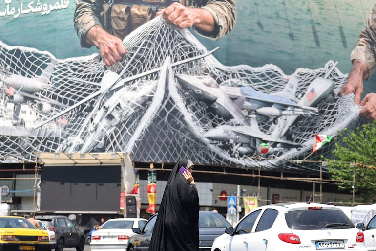 Una mujer pasa junto a una valla publicitaria gigante que dice "El estrecho de Ormuz permanece cerrado" en la Plaza de la Revolución en Teherán.