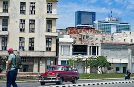 Un hombre camina por una calle mientras un auto pasa a su lado, con el hotel Iberostar Selection (C) y el hotel Habana Libre Melia (D) al fondo, en La Habana,