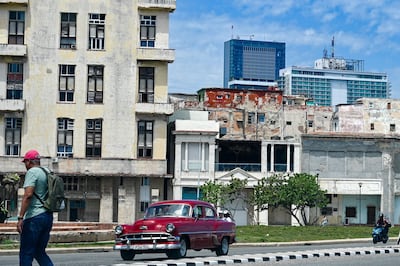 Un hombre camina por una calle mientras un auto pasa a su lado, con el hotel Iberostar Selection (C) y el hotel Habana Libre Melia (D) al fondo, en La Habana,