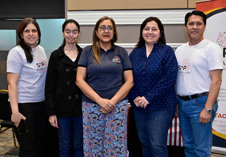 Cinco personas, tres mujeres y un hombre, sonríen en evento formal, luciendo camisetas con el logo 'SAP STATEALUMNI' en ambiente interior.