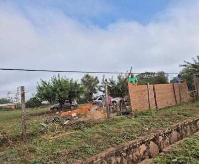 Hombres trabajando en muro, uno de rayas supervisa, otros dos construyen en la parte superior con ladrillos y tierra alrededor.