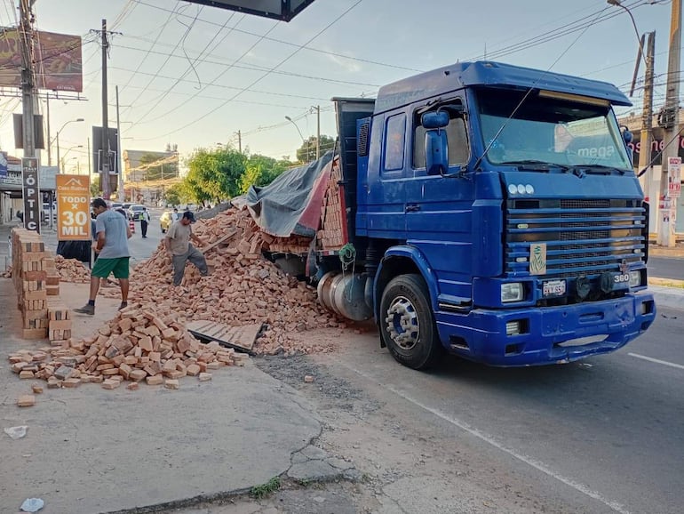 Dos hombres trabajan para despejar ladrillos en la avenida, mientras un camión azul parcialmente cubierto está en el fondo.
