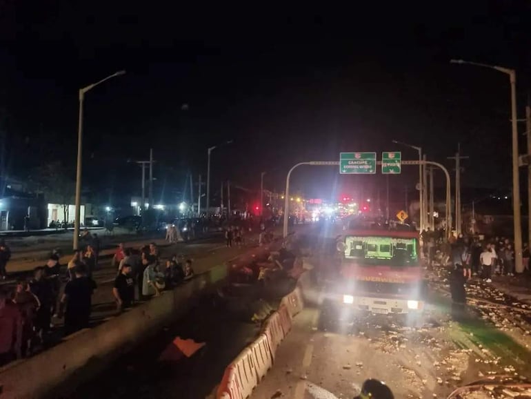 Grupo de personas en la carretera, rodeados de luces de vehículos y un camión de bomberos destacado.