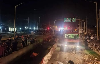 Grupo de personas en la carretera, rodeados de luces de vehículos y un camión de bomberos destacado.