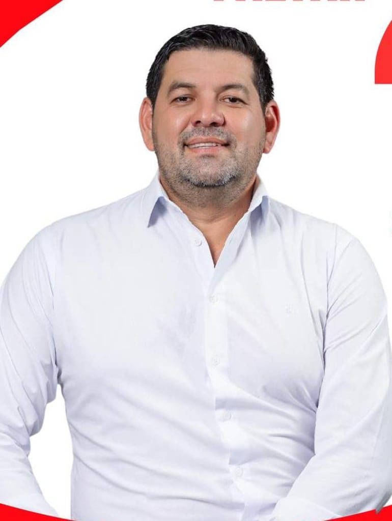 José Talavera, hombre de mediana edad con barba, sonríe vistiendo una camisa blanca, en un fondo simple con elementos gráficos rojos.