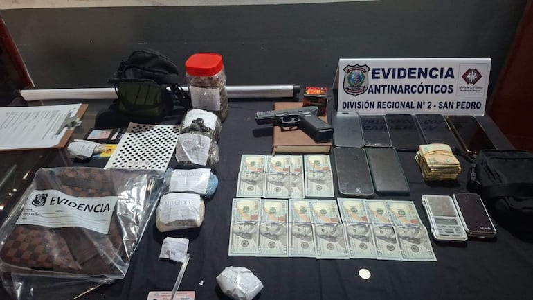 Mesa con objetos incautados: pistola, paquetes de sustancias, frasco y dinero en efectivo, en ambiente policial.