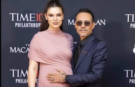 Nadia Ferreira con vestido rosa, mostrando su embarazo, y Marc Anthony en traje oscuro, ambos sonrientes en un evento elegante.