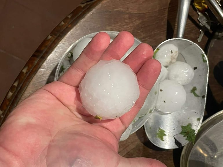 Mano sosteniendo granizo grande, con otros trozos en un recipiente metálico en un entorno de cocina.