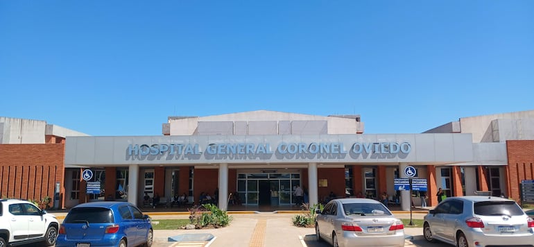 Fachada moderna del Hospital General Coronel Oviedo con vehículos estacionados y personas sentadas en la entrada.