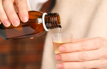 Una mujer sirve un jarabe en un vasito medidor.