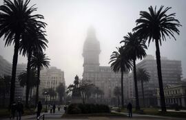 La gente camina por la Plaza Independencia mientras la niebla cubre el emblemático Palacio Salvo en Montevideo.