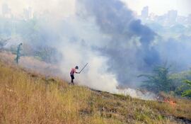 Un poblador de la zona, intenta aplazar el fuego que inició en el banco San Miguel y se extendió hasta la Costanera de Asunción.