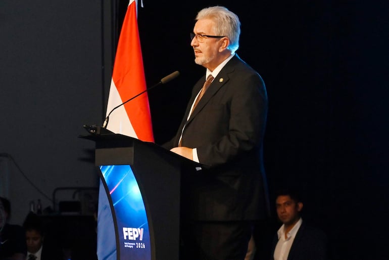 Hombre en el escenario con traje oscuro y corbata, frente a un atril con el logotipo de 'FEP 2026', flanqueado por la bandera de Paraguay.