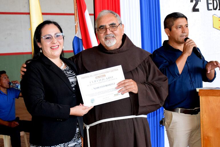 Clara Celenia Zacarías entrega un pergamino al fray y escritor moriniguense Marcelo Benítez.