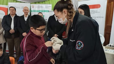 Niño en camiseta borgoña recibe tratamiento de salud por profesional con guantes, observados por adultos en un centro de salud.