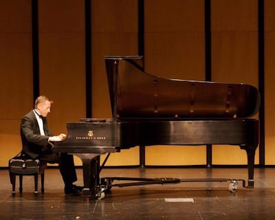 Daniel Luzko, vestido con frac, toca un piano Steinway & Sons en un escenario con paneles de madera.