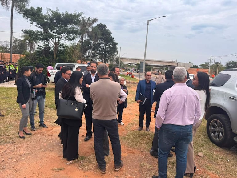Grupo de personas conversando en un terreno de construcción, con vehículos y oficiales de policía de fondo.