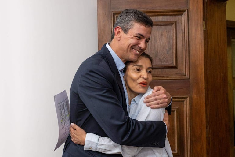 Santiago Peña en traje oscuro abraza a Rossana González, quien lleva blusa clara y sonríe. Ambiente interior institucional.