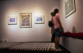 Mujer con blusa clara y bolso, y niña en camiseta rosa y pantalones cortos, observan cuadros en una galería iluminada.
