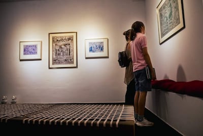 Mujer con blusa clara y bolso, y niña en camiseta rosa y pantalones cortos, observan cuadros en una galería iluminada.