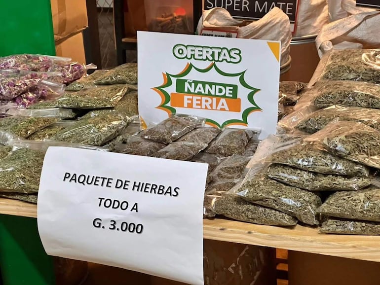 Mesa de madera con paquetes de hierbas variados y cartel de ofertas en un ambiente de mercado.