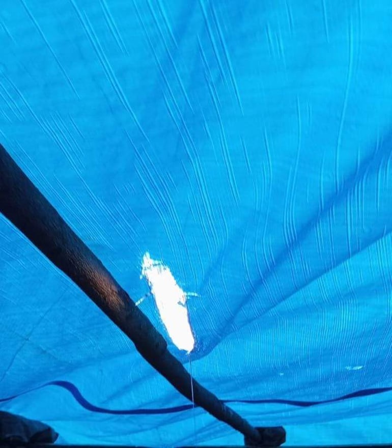Estructura cubierta con lona azul en un ambiente exterior, con luz filtrándose a través de un orificio en la lona.