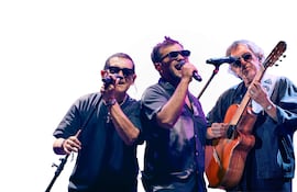 Músicos de Los Nocheros en el escenario, con gafas de sol y micrófonos, recreando una atmósfera de concierto musical.