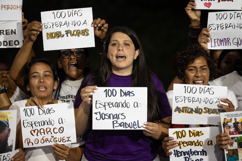 Personas sostienen carteles durante una vigilia afuera de la cárcel El Rodeo I este sábado, en Guatire (Venezuela).