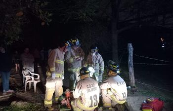 Bomberos en trajes de protección atienden a un hombre herido en el suelo en una escena de emergencia, con testigos observando.