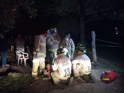 Bomberos en trajes de protección atienden a un hombre herido en el suelo en una escena de emergencia, con testigos observando.