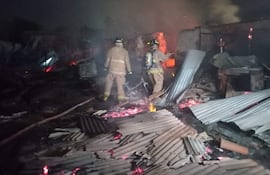 Dos bomberos equipados con trajes de protección y cascos, rodeados de escombros y humo tras un incendio.