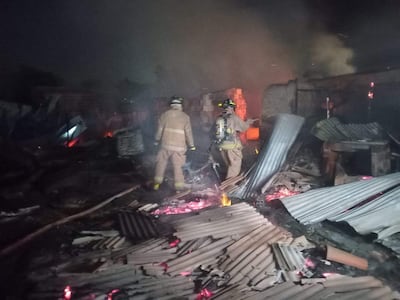 Dos bomberos equipados con trajes de protección y cascos, rodeados de escombros y humo tras un incendio.